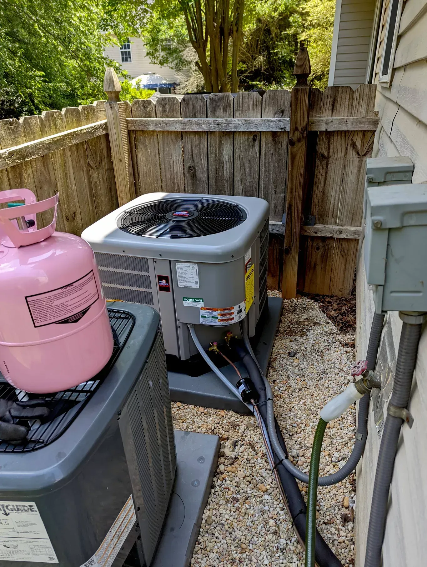 Two air conditioners are sitting next to each other on the side of a house.