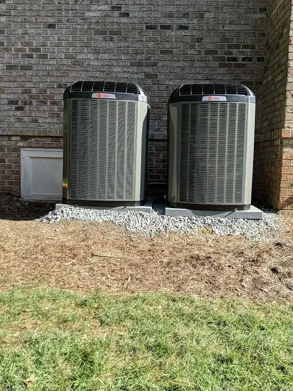 Two air conditioners are sitting next to each other on the side of a brick building.