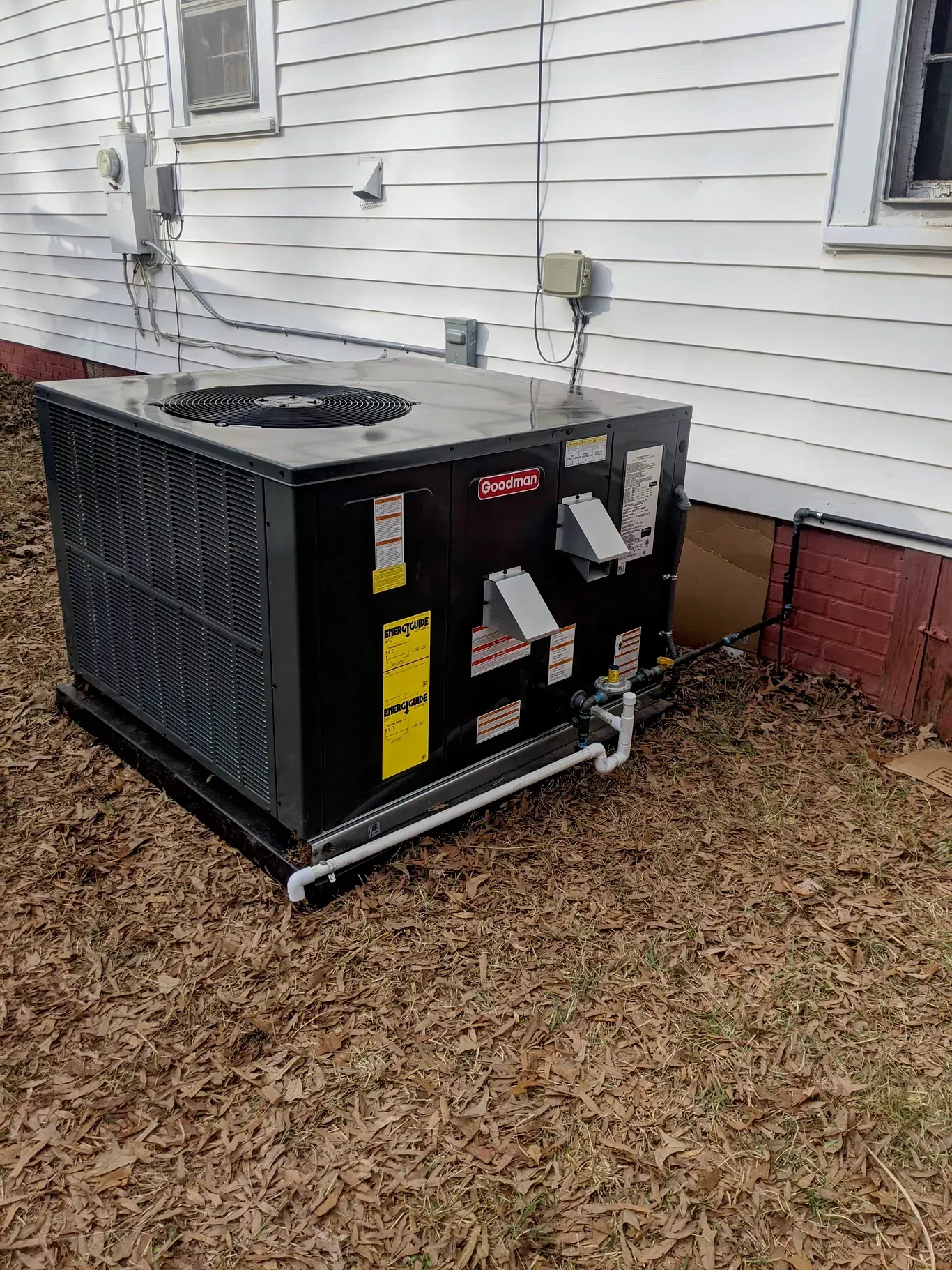 A black air conditioner is sitting in front of a white house.