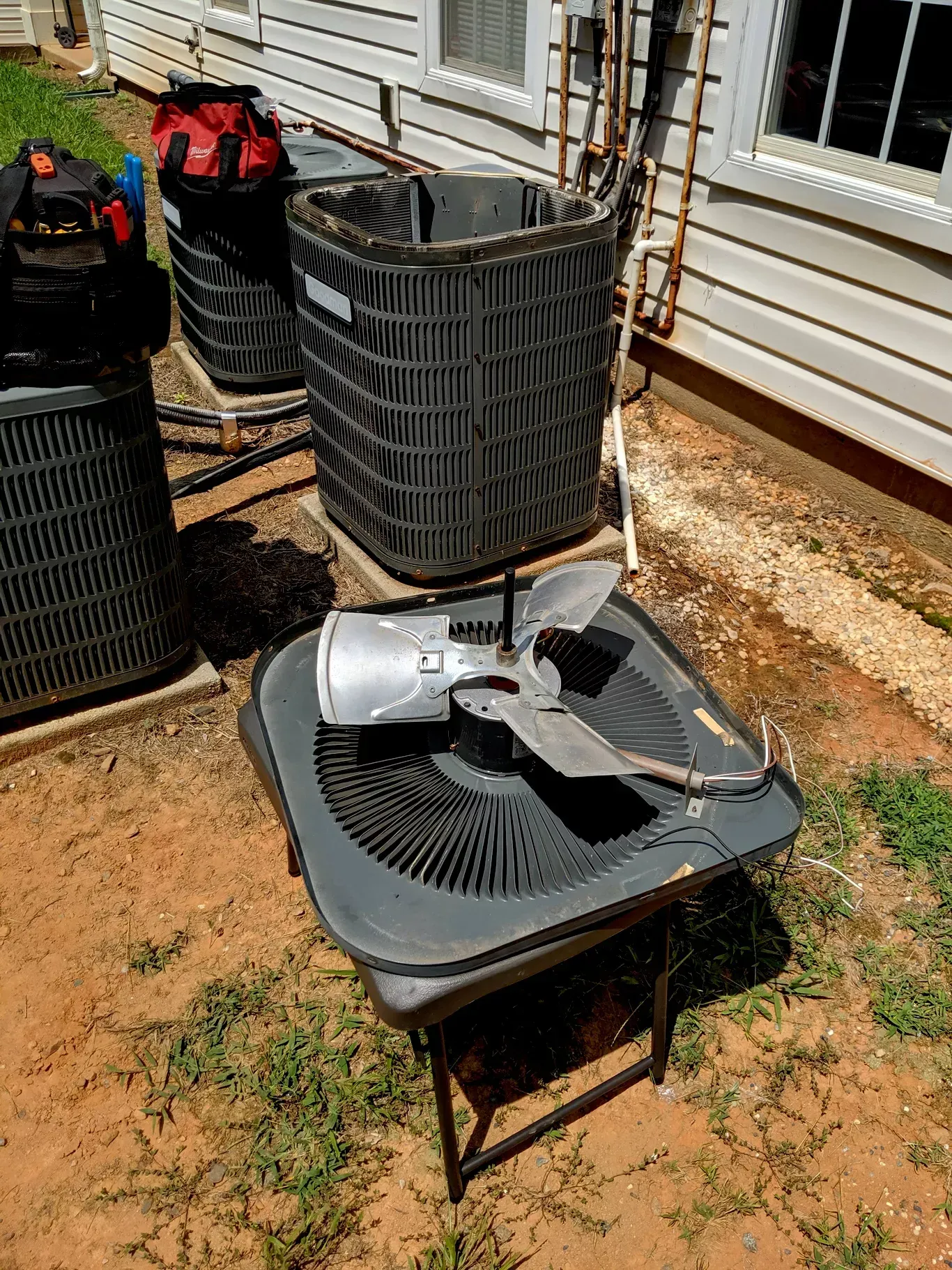 A fan is sitting on top of an air conditioner outside of a house.