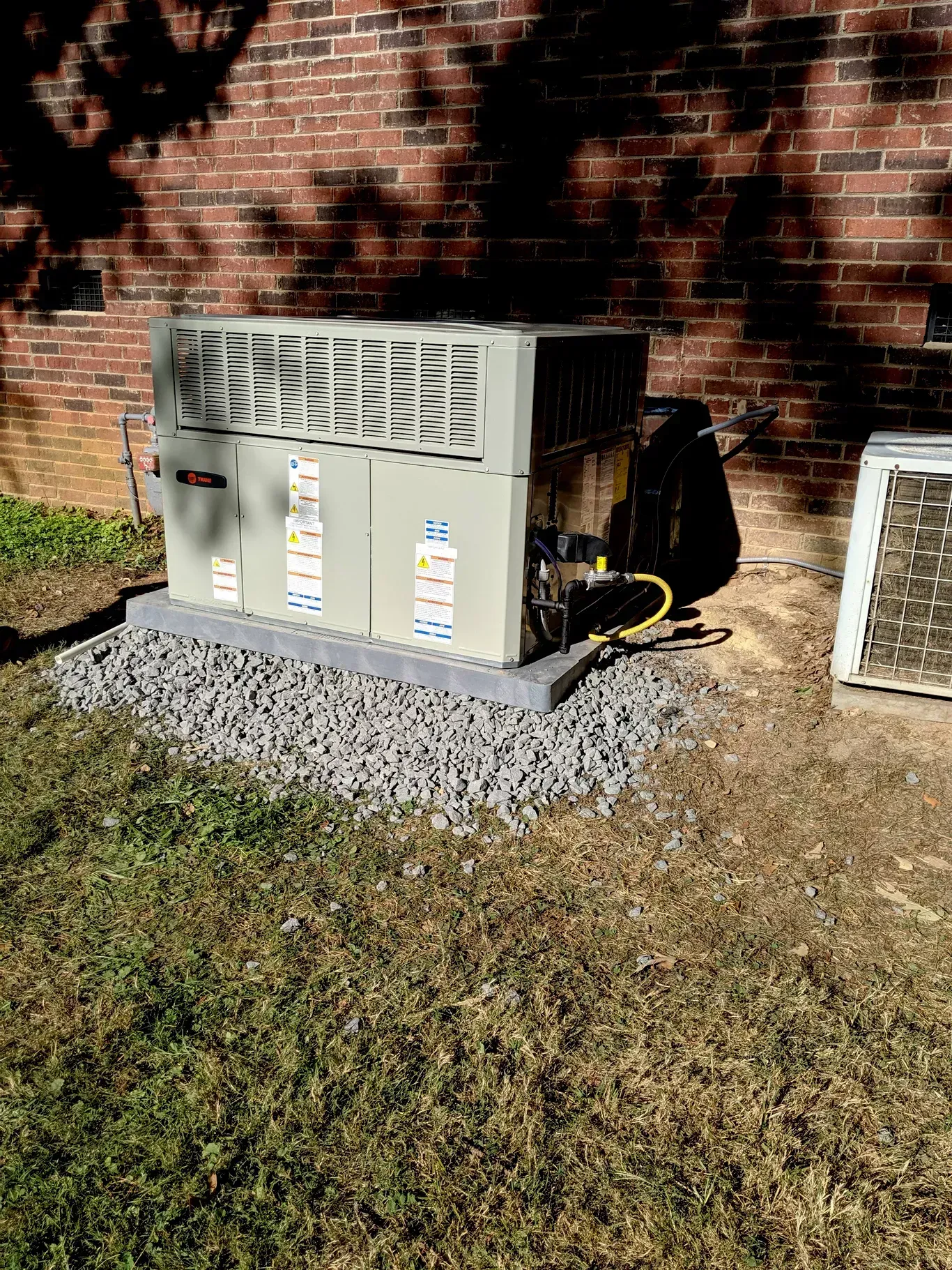 An air conditioner is sitting in the grass in front of a brick building.