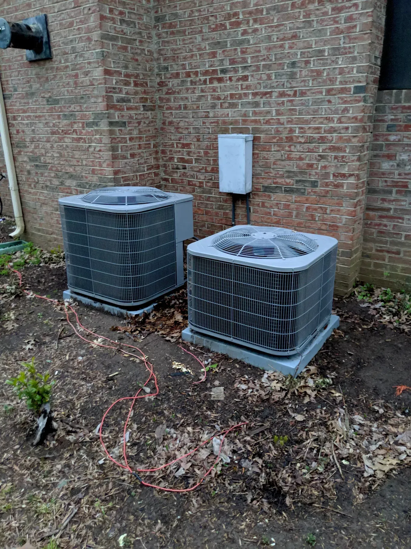 Two air conditioners are sitting next to each other on the side of a brick building.