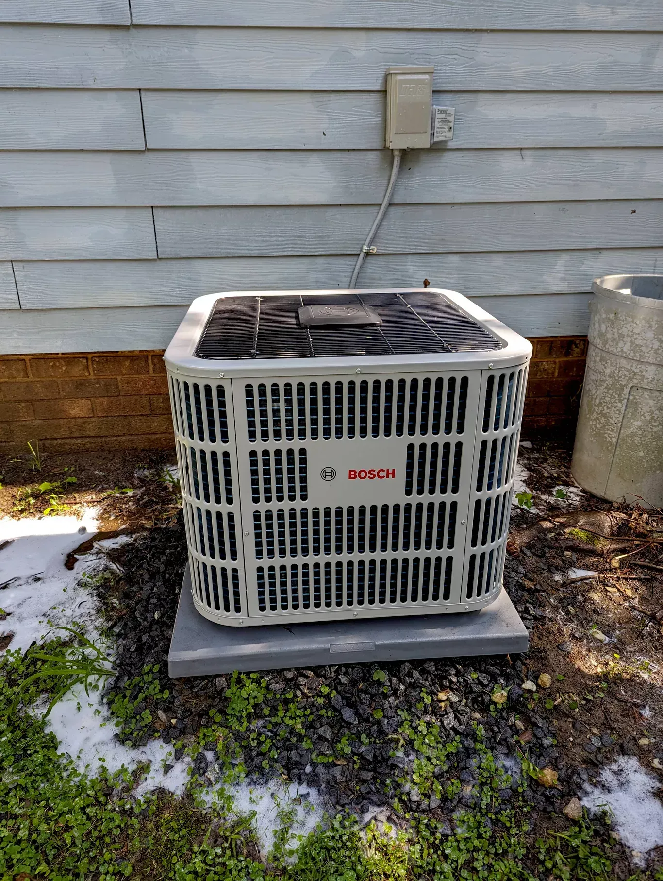 A bosch air conditioner is sitting outside of a house.