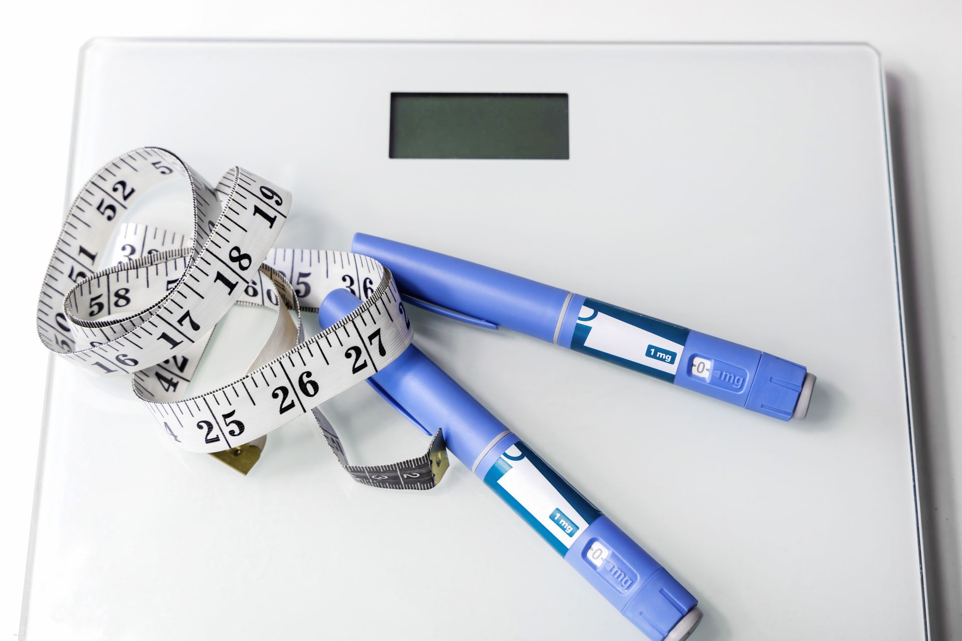 White scale with measuring tape and two blue injection pens. White scale with measuring tape and two blue injection pens.