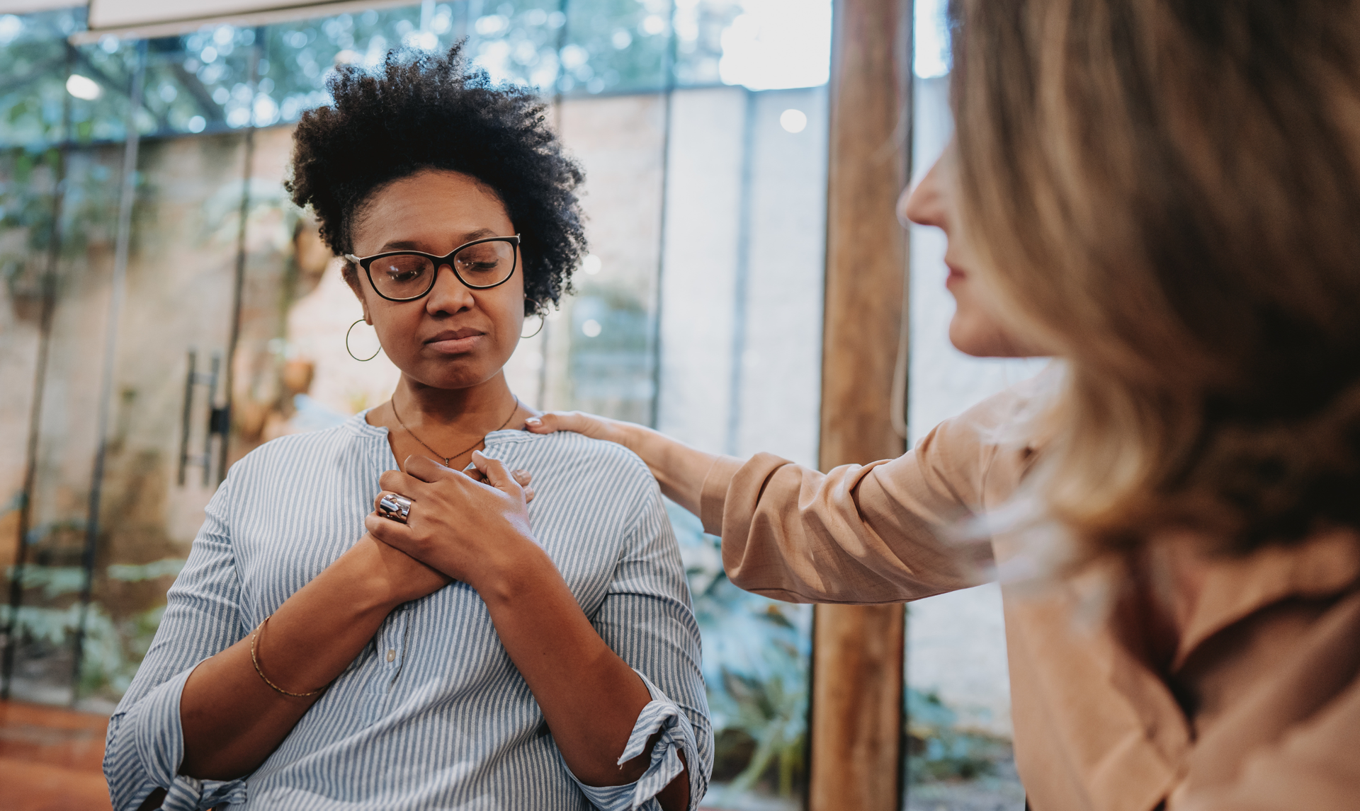 Woman comforted by another with hand on her shoulder, indoors.