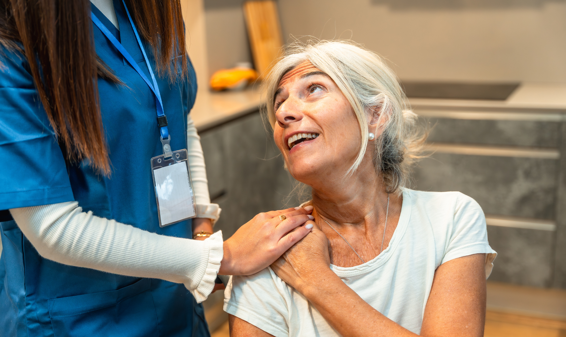 Nurse comforting an elderly person with a hand on the shoulder; interior setting, positive expressions.