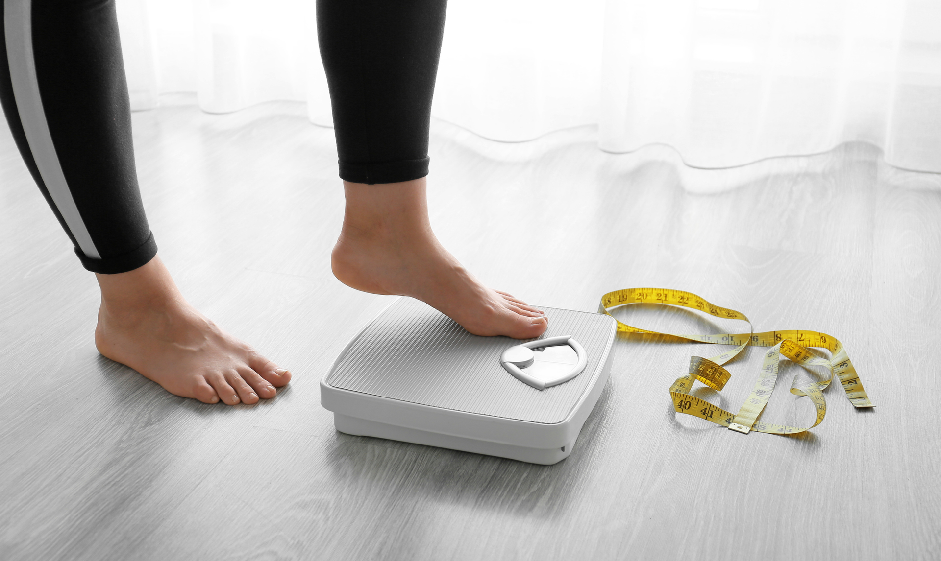 Person stepping on a digital scale, with a measuring tape on the floor. Person stepping on a digital scale, with a measuring tape on the floor.