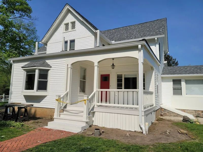 White house with porch and red door; brick walkway leads to the front steps.