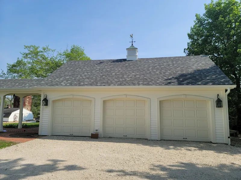 White three-car garage with matching arched doors under a blue sky; gravel driveway.
