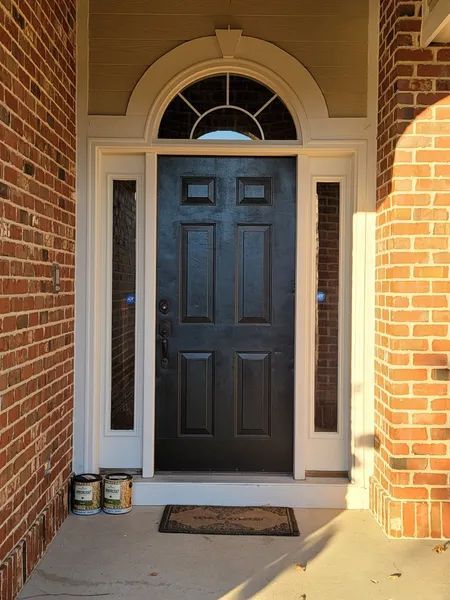 Black front door with arched transom, sidelights, white trim, and brick facade.