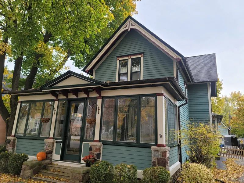 Green house with porch and trees, autumn foliage.