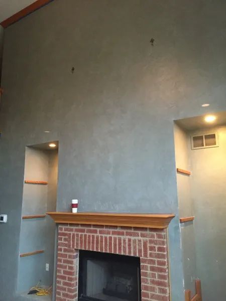 Fireplace with brick hearth, gray wall, recessed shelves, and two lights.