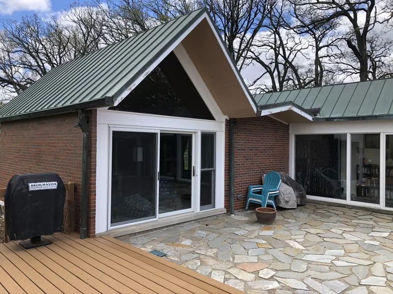 A brick building with a green metal roof, large sliding glass doors, and a stone patio.