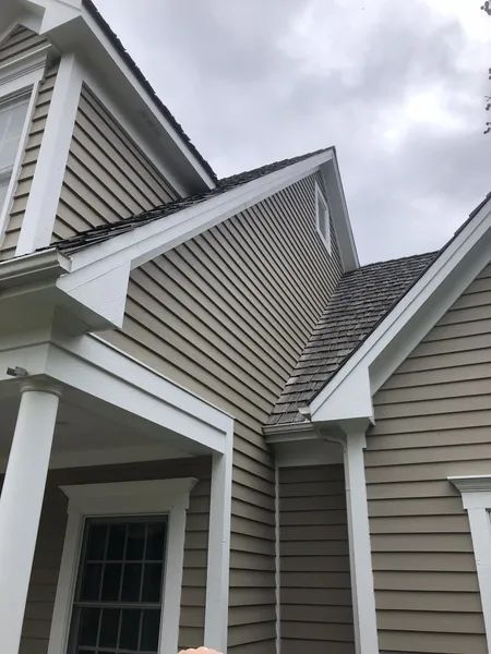 Beige siding on a house with white trim, gray roof, and cloudy sky.