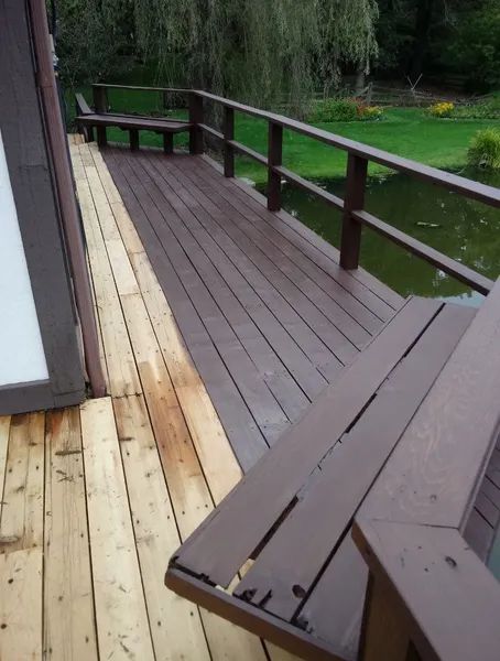 Brown stained deck with railings and bench overlooks a pond. Partially unstained deck in foreground.