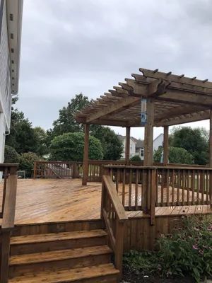 Wooden deck with pergola, stairs, and railing. Overcast sky, trees, and house in background.