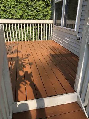 Brown wooden deck with white railing, against a house. Sunny day.