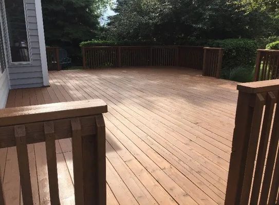 Wooden deck with brown stain and railing. Green trees in the background.