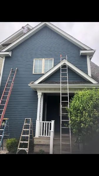 Blue house exterior with ladders leaning against the siding, a white portico and a bush to the right.