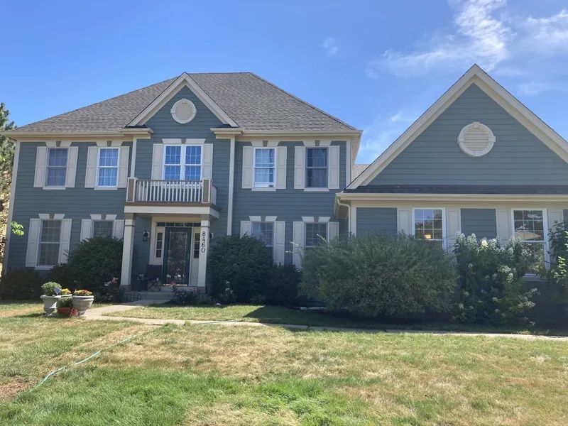 Two-story blue house with white trim, shutters, and a balcony. Green lawn and blue sky.