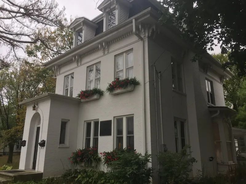 White two-story house with flower boxes and dormers; trees in the background.