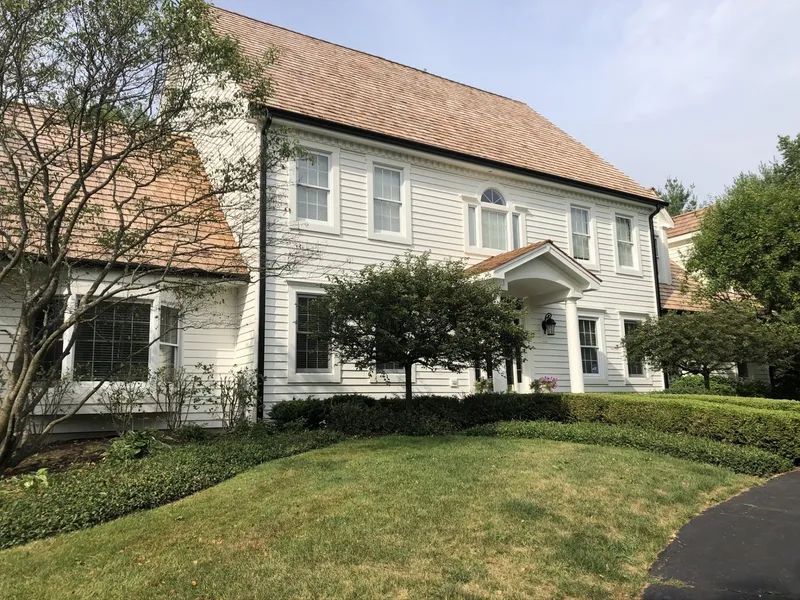 White house with brown roof, lawn, trees, and a driveway.