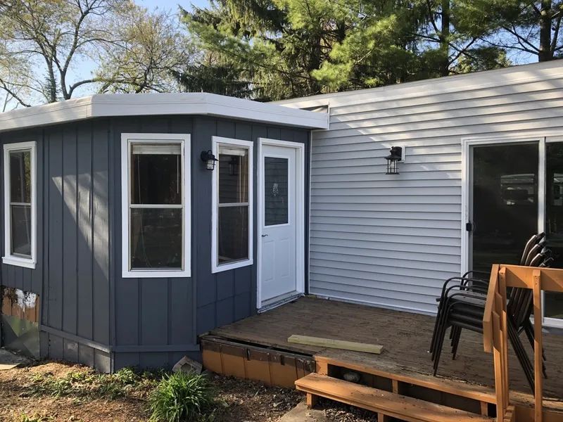Exterior view of a house with a grey siding and an attached blue-grey extension with a door and windows.