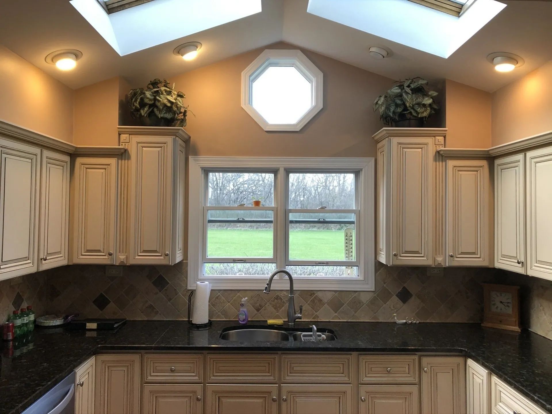 Kitchen with light cream cabinets, black countertop, and window overlooking a green lawn.