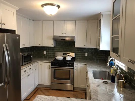 White kitchen with stainless steel appliances, green tile backsplash, and light-colored countertops.