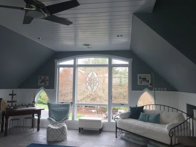 Room with large window, gray walls, white ceiling, furniture, and tree view.