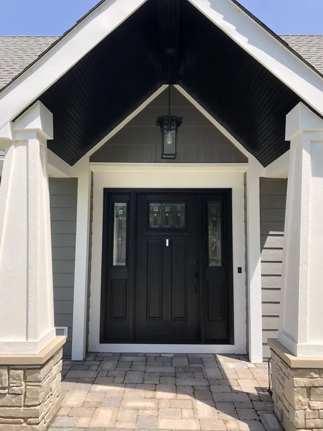Black front door with sidelights under a gabled entryway with white pillars and dark ceiling.