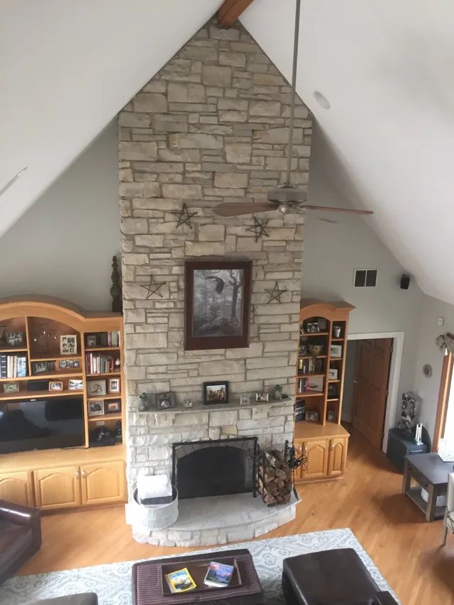 Stone fireplace in a high-ceiling living room, flanked by wooden built-ins. Dark framed picture above the mantel.