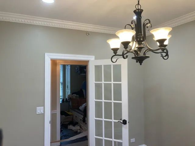 A chandelier hangs above a doorway with glass panels in a room with crown molding and light green walls.