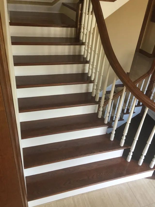Wooden staircase with dark treads, white risers, and a curved railing.