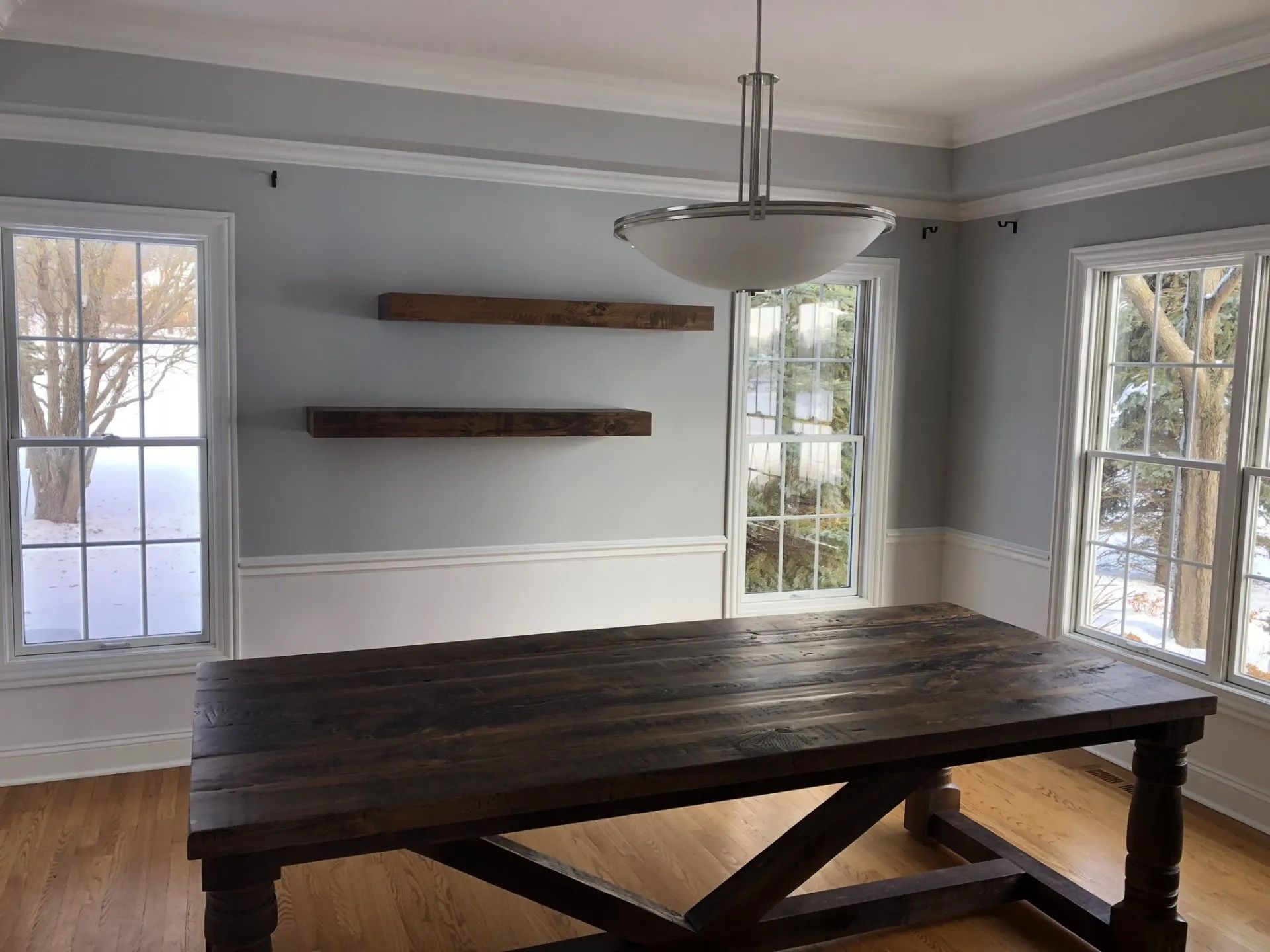 Dining room with a dark wood table, floating shelves, and snow-covered windows.