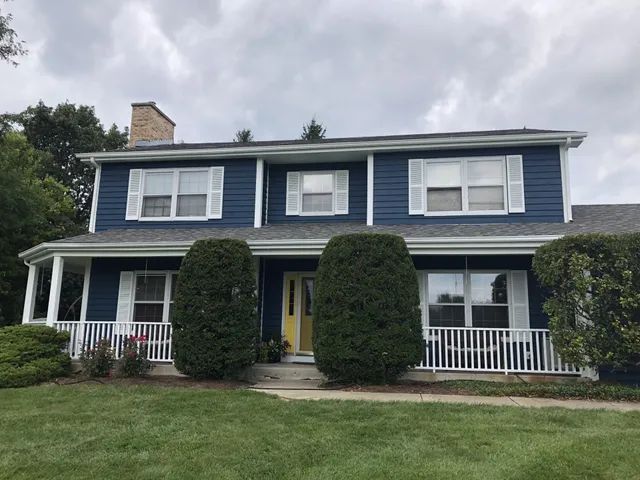 Blue house with white trim, shutters, and porch, featuring a yellow door.
