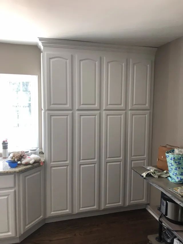 White kitchen cabinets filling a wall, next to a window and a counter with items.