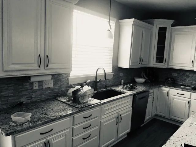 Black and white photo of a white kitchen with cabinets, a sink, and countertops.
