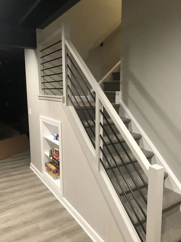 Staircase with white banisters, black metal bars, and a built-in shelf with items.