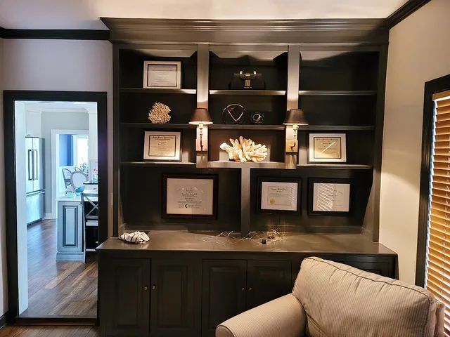 Dark gray built-in cabinet with shelves, lamps, awards, and decor; doorway to the left.