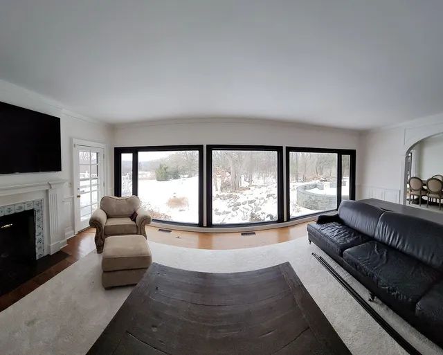 Living room with large windows, fireplace, sofa, chair, and snow-covered outside view.