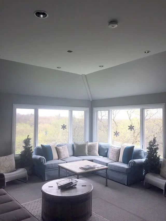 Cozy sunroom with a sectional sofa, large windows, and a round coffee table.