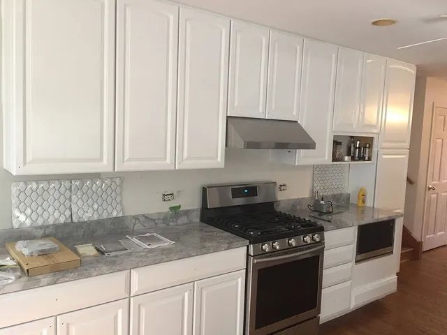 White kitchen cabinets with stainless steel appliances, marble countertops, and decorative tile backsplash.