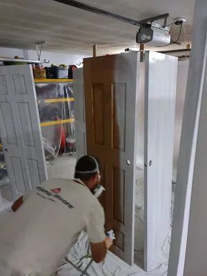 Man spray painting a door white in a garage.