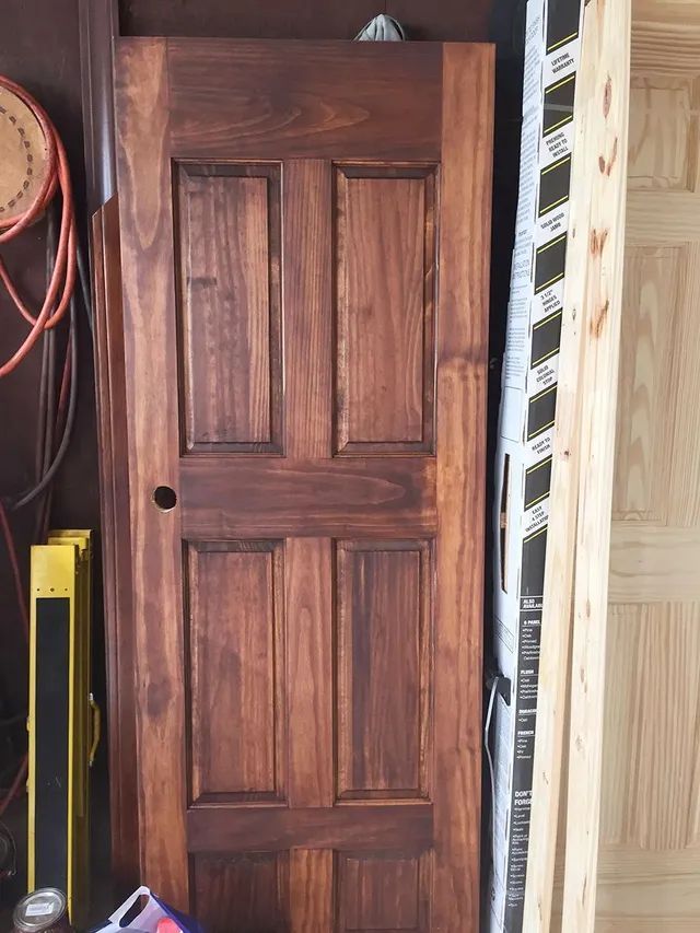 Stained brown wooden door with four rectangular panels, leaning against other materials.