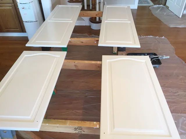 Four white cabinet doors laid flat on a wooden table, possibly for painting.