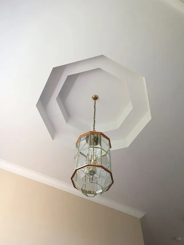 Octagonal ceiling with chandelier. The ceiling is white with molding and the chandelier is glass and gold.