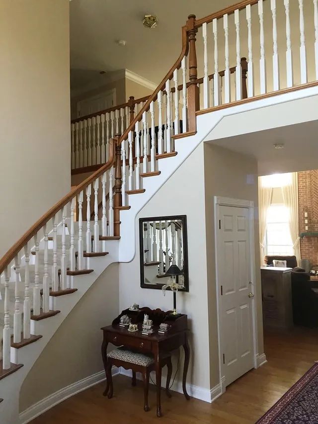 Two-story foyer with wooden staircase, white banister, and antique desk and mirror.