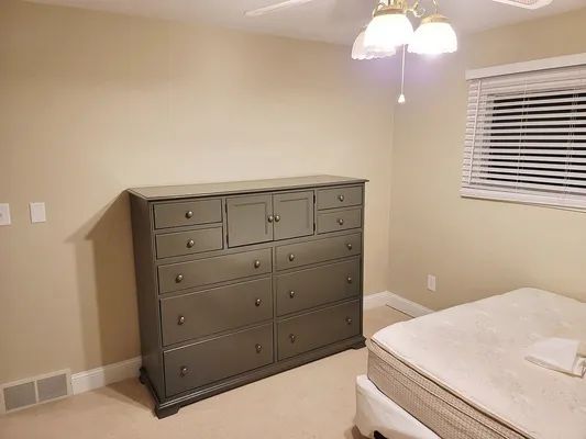 Bedroom with gray dresser, bed, blinds, and beige walls.