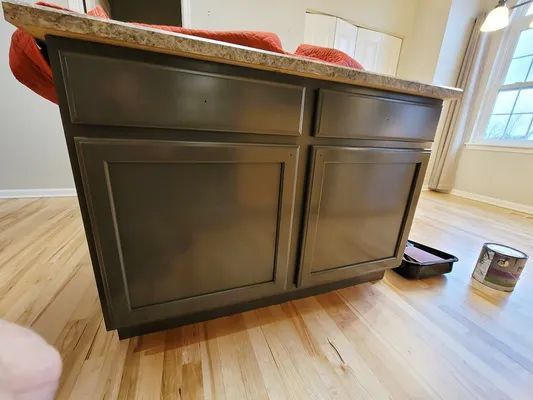 Brown painted kitchen island with countertop, on wooden floor, near window.